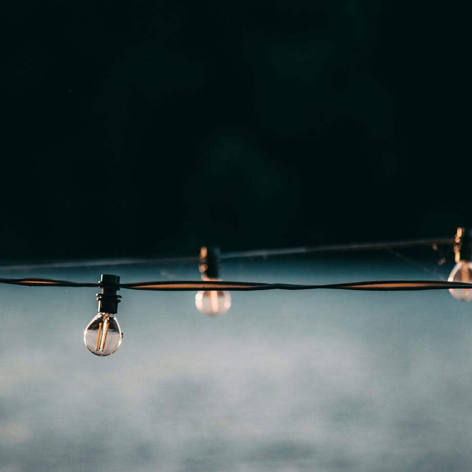 Small switched off electric lamps on long wire strained above gray blurred surface